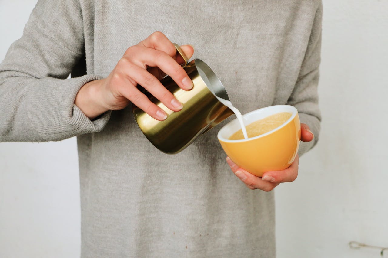 A person pouring milk into a coffee cup, showcasing a warm and cozy moment.